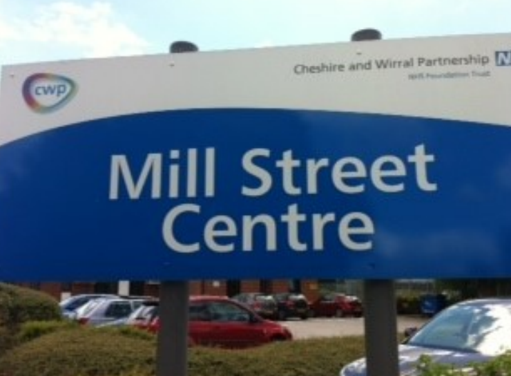 A photograph of a sign which reads 'Mill Street Centre'. It also has the Cheshire and Wirral Partnership NHS Foundation Trust logo in the top right corner of the sign.