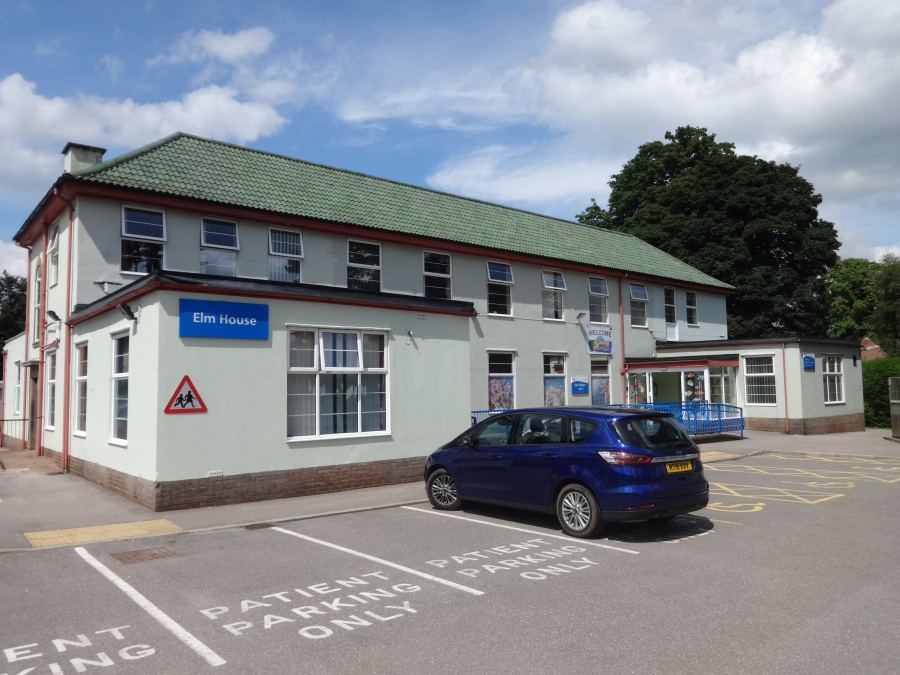 A photograph of the outside of Elm House - a large white building - and the car park at the front of the building, with one car parked outside